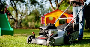 Man mowing the lawn with a push mower with children's backyard toys in the background