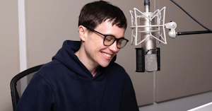 Elliot Page in a black sweatshirt smiling while sitting at a mic.
